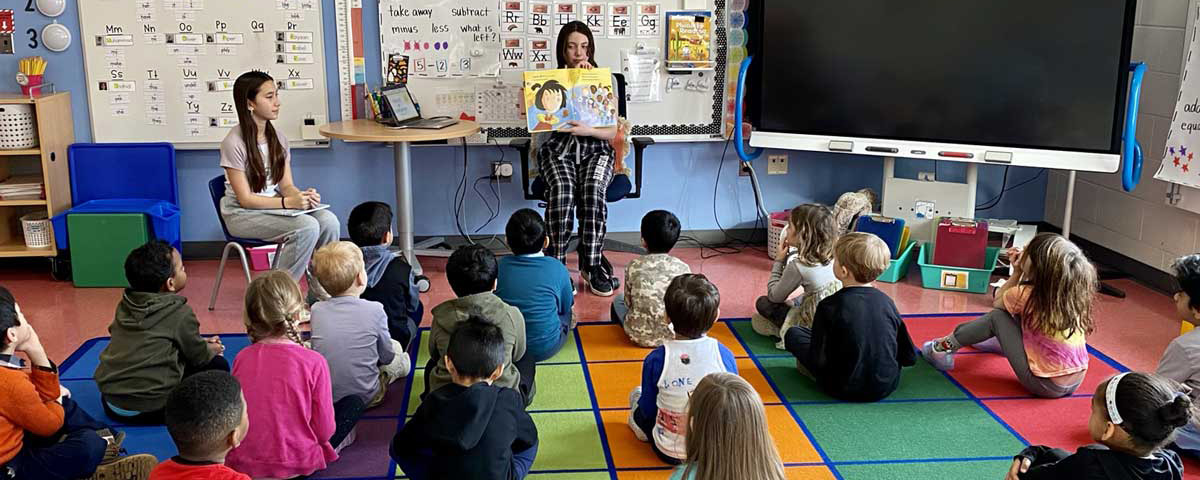 Photo of middle school student reading to kindergarten students