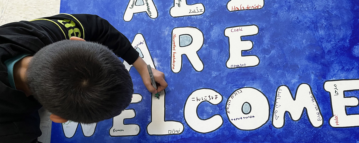 Photo of student writing "welcome" on a blue banner