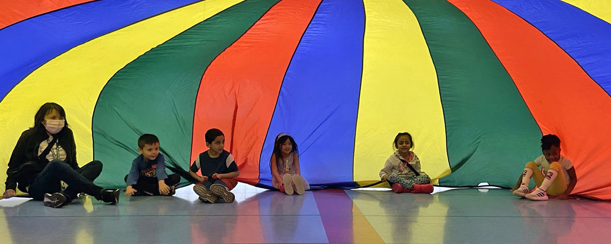 Photo of students seated under a multicolor parachute in P.E. class